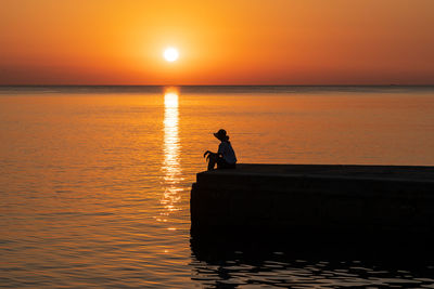 Silhouette man sitting on boat on sea against sky during sunset