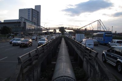 Vehicles on road by buildings against sky in city