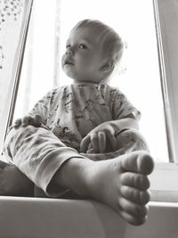 Cute baby girl sitting on window at home