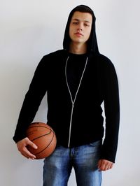 Portrait of man with basketball standing against wall