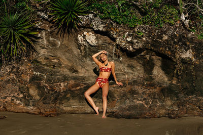 Beautiful young woman wearing bikini against rock formation at beach