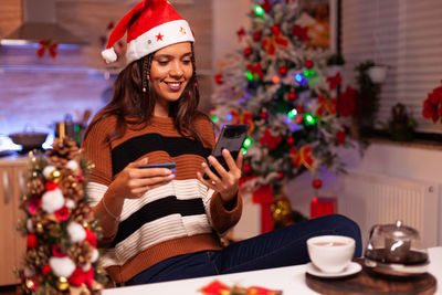 Portrait of smiling woman with coffee while sitting on christmas tree