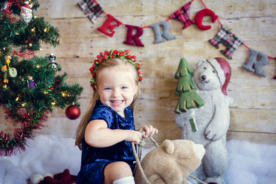 Portrait of cute girl sitting with teddy bear against wall at home