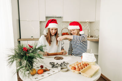 Two charming sisters in santa claus hats bake cookies for christmas in the kitchen. 