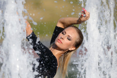 Beautiful woman with hand raised standing against fountain