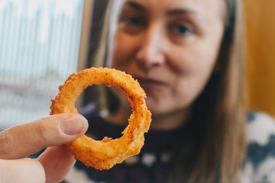 Portrait of woman holding onion ring while sitting at cafe