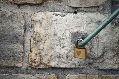 Close-up of love lock on railing against stone wall
