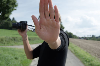 Close-up of man photographing while gesturing stop sign against sky
