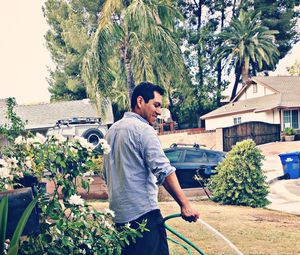 Rear view of smiling man holding garden hose while standing in yard