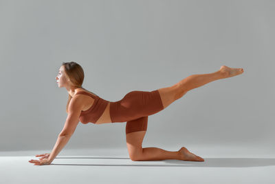 Side view of woman exercising against white background