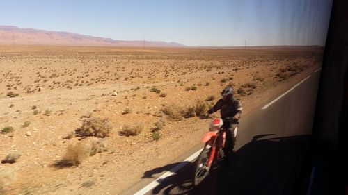 Rear view of man riding motorcycle on desert against sky