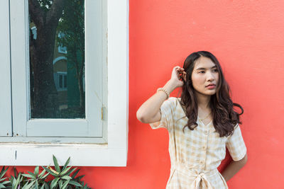 Young woman standing against red wall