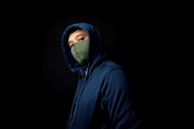 Portrait of young man standing against black background