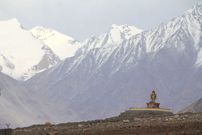 Scenic view of buddha idol and snowcapped mountains against sky