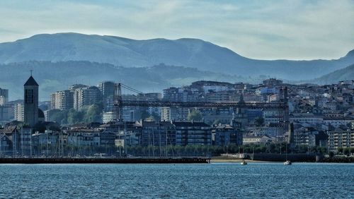 View of city at waterfront against cloudy sky