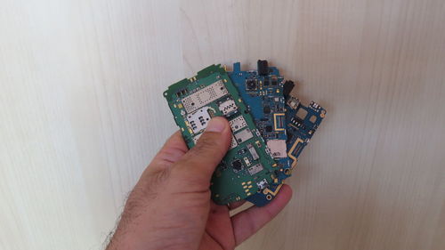Cropped hand of man holding mobile phone circuit board