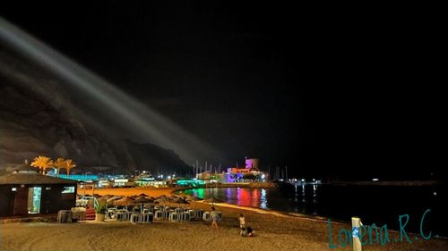 Illuminated city by sea against sky at night