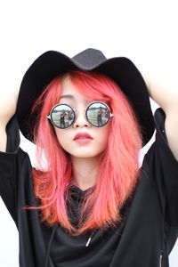 Portrait of beautiful woman wearing sunglasses and hat standing against white background