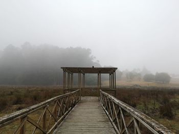 Footbridge over foggy weather against sky