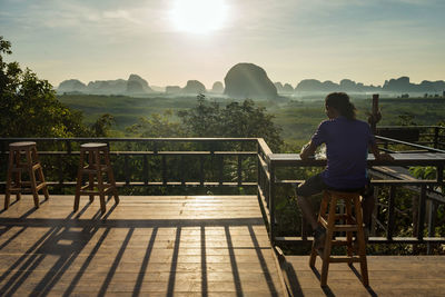 Rear view of man sitting on railing against mountain