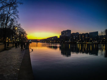 River by illuminated buildings against sky at sunset