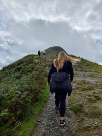 Rear view of woman walking on mountain trail against sky