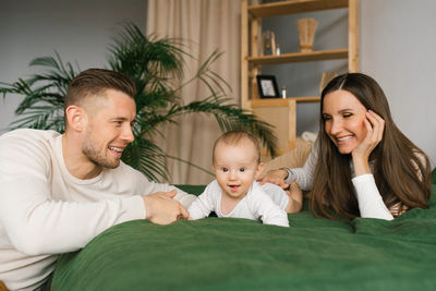 Happy family with smiles and a baby are lying and resting on the bed in their house