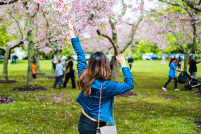 Rear view of woman with arms raised standing in park