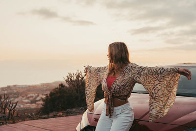 Rear view of young woman standing against sky during sunset