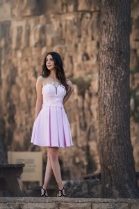 Full length of smiling young woman in purple dress standing against mountain