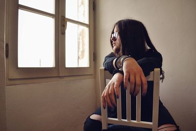 Young woman looking away while sitting on window at home