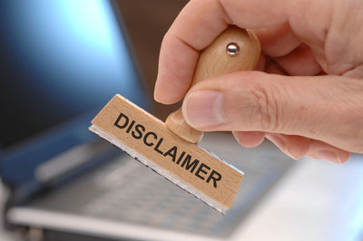 Cropped hand holding rubber stamp with disclaimer text at office