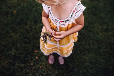 Low section of girl holding dry leaves while standing on grass