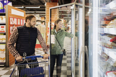 Couple buying groceries while standing at refrigerated section