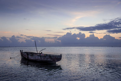 Boat moored in sea against sky during sunset