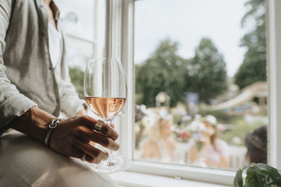 Midsection of young man holding wineglass sitting near window in cafe