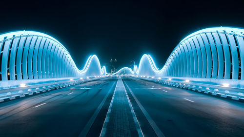Light trails on bridge against blue sky at night