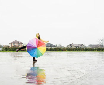 Beautiful brunette woman in yellow raincoat holding rainbow umbrella out in the rain