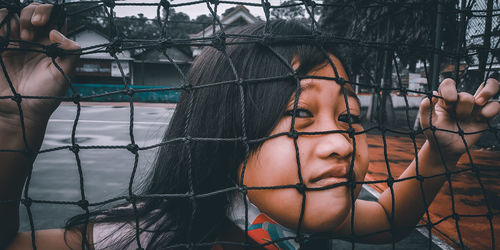 Close-up portrait of young woman standing by fence