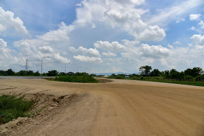 Dirt road amidst field against sky