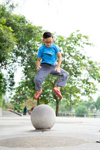 Outdoor portrait of a cute malaysian little boy trying to jump from a concrete ball at the park.