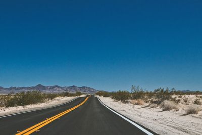 Road passing through landscape against clear blue sky