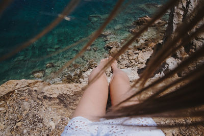 Low section of woman sitting on rock against sea