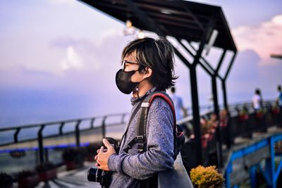 Side view of woman standing by railing against sky