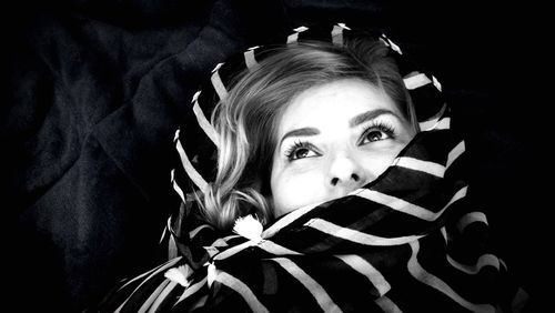 Thoughtful woman wrapped in scarf lying on bed