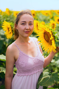 Portrait of young woman standing against sunflowers