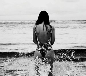 Rear view of woman standing at beach against sky