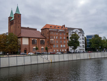 Buildings by river against sky