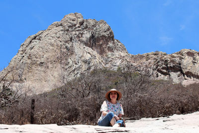Full length of woman sitting on rock against sky