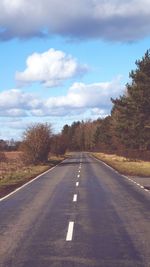 Empty road along trees and against sky